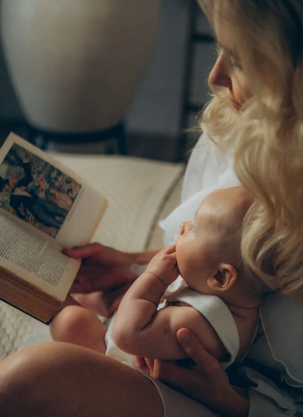 Eine Mutter liest ein Buch und hält dabei ihr Baby.