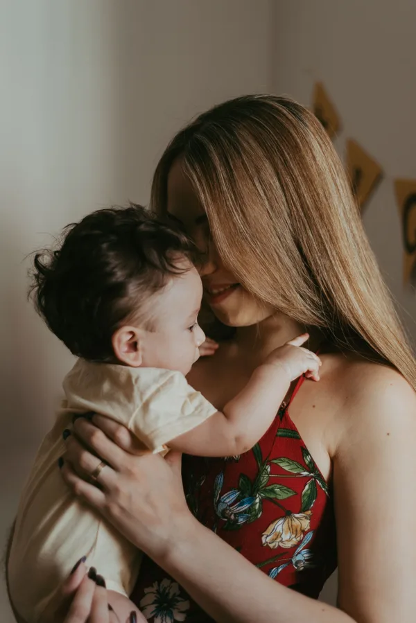 Eine Mutter hält ihr waches Baby nah bei sich und lächelt es an.